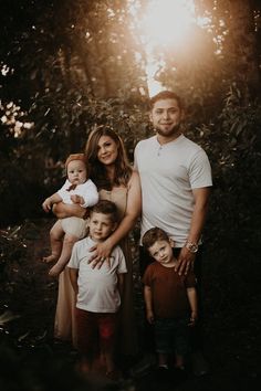 a family posing for a photo in front of some trees with the sun shining down on them