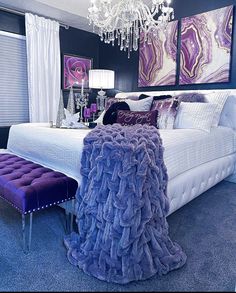 a bed with purple and white decor in a bedroom next to a chandelier