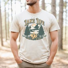 Our retro and stylish Lake Life tshirt is perfect for those summer vacations at the lake. Whether you are lounging around on the beach at your cabin or cottage, or enjoying some quiet time paddle boarding on the lake, this tshirt will keep you cool and comfortable. The simple mountain, campfire and pine tree design is perfect for camping and hiking in the Rockies. It makes a great gift for outdoor enthusiasts or anyone that wants to relive days at the lake. Made with lightweight and breathable fabric, this tshirt ensures comfort even in warm climates. The sleeveless design allows for easy movement and keeps you cool as you embark on your summer adventures. High quality print makes it an ultimate statement shirt for years to come. This item has side seams to provide structural support. All Outdoor Short Sleeve T-shirt For Summer, Outdoor Short Sleeve T-shirt With Front Print, Summer Outdoor Cotton T-shirt, Summer Outdoor Top With Letter Print, Summer Outdoor Tops With Letter Print, Summer Tops With Letter Print For Outdoor, Summer Adventure T-shirt With Short Sleeves, Outdoor Summer T-shirt With Screen Print, Summer Outdoor Screen Print T-shirt