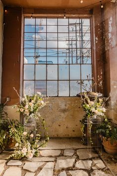 two vases filled with flowers sitting in front of a window on top of a stone floor