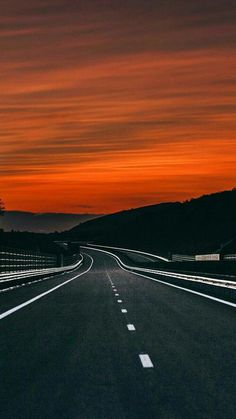 an empty road with the sun setting in the background