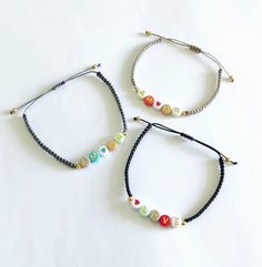 three bracelets with beads on them sitting on a white surface, one is black and the other has multicolored beads