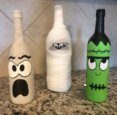 three decorated wine bottles sitting on top of a counter next to each other, with eyes and noses painted on them