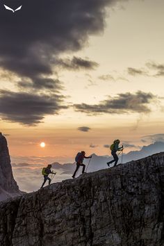 three hikers climbing up the side of a mountain at sunset, with mountains in the background