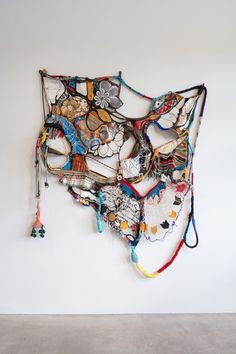 a sculpture made out of various objects hanging on the wall in front of a white wall