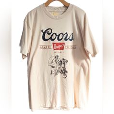 Coors Banquet Beer T-Shirt Featuring A Cowboy With Lasso & Horse Pencil Drawing. Intentionally Distressed For A Vintage Vibe. Text Reads "Coors Banquet" "Golden Colorodo" "Est 1873". A Simple, Pleasant Design On A Delightfully Oatmeal-Colored Shirt. Official Coors Licensed Product Printed On A Quality Teeluv Shirt. 100% Cotton. New With Tag. American Golden Mountains Lager Alcohol Usa Co U.S.A. U.S. United States Of America Alcoholic Bar Beverage Golden Colorado Bar Drinking Games Pbr College Pong Dad Humor Party Fun Pub Garden Oktoberfest Brewery Microbrewery America Alcohol Budweiser Bud Moon Natural Light Michelob Ultra Anheuser-Busch Miller High Life Yuengling Pabst Blue Ipa Bier Ri Vintage Beige Short Sleeve T-shirt, Cream Vintage T-shirt With Relaxed Fit, Retro Cream Short Sleeve T-shirt, Vintage Cream Short Sleeve T-shirt, Retro Beige Short Sleeve T-shirt, Vintage Cream T-shirt For Summer, Vintage Short Sleeve Cream T-shirt, Retro Beige Crew Neck T-shirt, Vintage Cream Tops With Letter Print