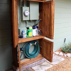 an open wooden box on the side of a house with hoses and other items in it