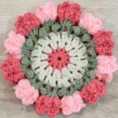 a crocheted circular with pink and green flowers in the center on a wooden surface