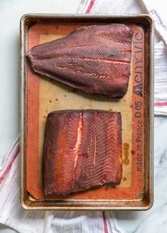 two pieces of fish sitting on top of a baking pan next to a towel and spoon