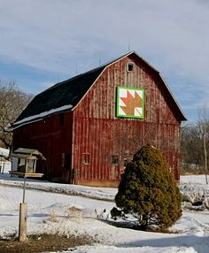 a red barn with a green and white quilt hanging from it's side in the snow