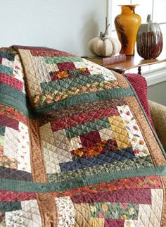 a quilted blanket sitting on top of a couch next to a vase filled with flowers