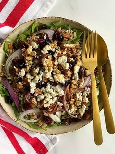 a salad in a bowl on top of a red and white striped table cloth next to a gold fork