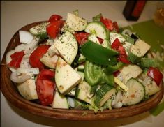 a wooden bowl filled with cucumbers, tomatoes and onions on top of a table