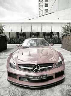 a pink sports car parked in front of a tall building with plants on the roof