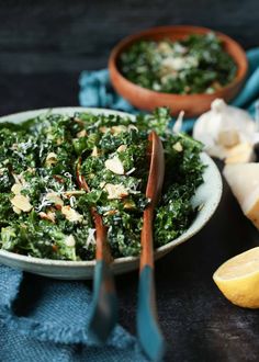 a bowl filled with greens next to two lemon wedges and garlic on a table