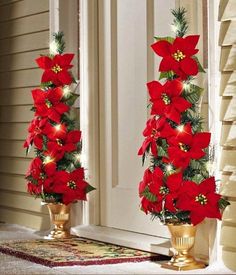 two gold vases with red poinsettias and greenery on the side of a house