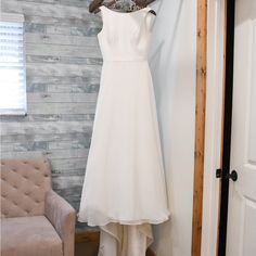 a wedding dress hanging on a hanger in a room with a chair and window