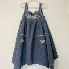 This Beautiful Size 5 Chambray Blue Easter And Spring Sundress Was Never Worn. We Did Remove Tags In Prep For Wearing But My Little Now Has A “No Dresses” Rule So This Poor Beauty Is Just Sitting In The Closet. The Dress Is Of Chambray Blue Fabric Throughout With A Handkerchief Hem. The Adorable White Embroidered Detail Along The Top Give The Dress A Slight Boho And Feminine Touch. Additional Detail Include Two Front Pockets With Embroidery And A Keyhole Back With A Brass Colored Button Secured Embroidered Light Blue Cotton Dress, Light Blue Embroidered Cotton Dress, Blue Cotton Dress With Floral Embroidery, Blue Cotton Dress With Embroidered Hem, Cute Blue Embroidered Dress, Blue Cotton Embroidered Beach Dress, Blue Cotton Embroidered Dress For Beach, Blue Sleeveless Embroidered Beach Dress, Light Blue Embroidered Sleeveless Dress