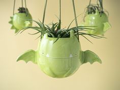 three green planters with plants in them hanging from hooks on a wall or ceiling