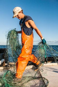 a man in an orange overalls and hat is pulling some fishing nets