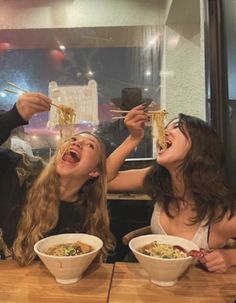 two women eating noodles with chopsticks at a restaurant