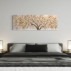 a bed with two lamps on either side and a painting above it that has a tree in the middle