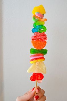 a person is holding up a rainbow lollipop with gummy bears on it