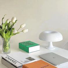 a white table topped with books and a vase filled with flowers next to a laptop computer