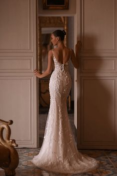 a woman in a wedding dress is standing near a door and looking at the mirror