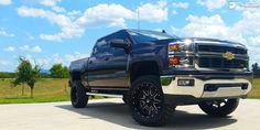 a large black truck parked on top of a parking lot next to a lush green field