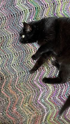 a black cat laying on top of a colorful blanket covered in crocheted yarn