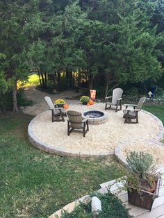 an outdoor fire pit surrounded by lawn chairs and graveled area with trees in the background