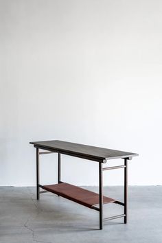 a wooden table with metal legs and a shelf on the top, against a white wall