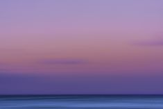 an airplane is flying over the ocean at sunset or dawn with purple and blue hues