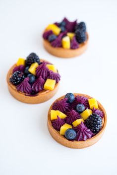 three small desserts with fruit on top of each one are sitting on a white surface