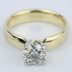 a yellow gold engagement ring with a round brilliant diamond in the center, on a white background