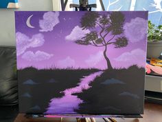 an easel with a painting on it sitting in front of a window that has purple sky and clouds