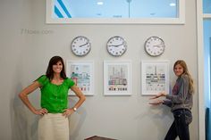 two women standing next to each other in front of clocks and pictures on the wall