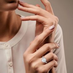 a woman in white shirt holding onto her finger and wearing a ring with a diamond on it