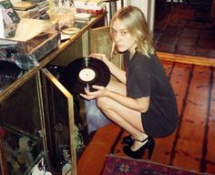 a woman sitting on top of a wooden floor next to a glass case filled with records