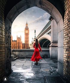 a woman in a red dress is walking through an archway with the big ben clock tower in the background