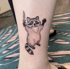 a small raccoon tattoo on the ankle with a knife in it's hand