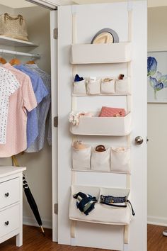 a white closet with hanging baskets and clothes on the door shelf, next to a dresser