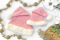 two pink and white knitted mittens next to some beads on a table with flowers