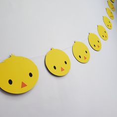 a bunch of little yellow chicks hanging from a line on a white wall with string