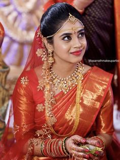 a woman in red and gold sari with jewelry on her head, posing for the camera