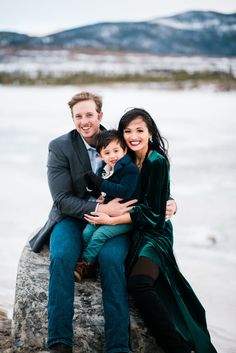 a man, woman and child sitting on a rock by the water