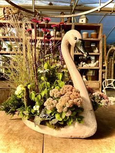 a swan planter with flowers and plants in it's back end on a table