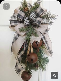 a christmas wreath with bells and pine cones hanging from the front door, decorated with plaid ribbon