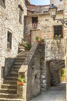 an old stone building with stairs leading up to the second floor and potted plants on either side